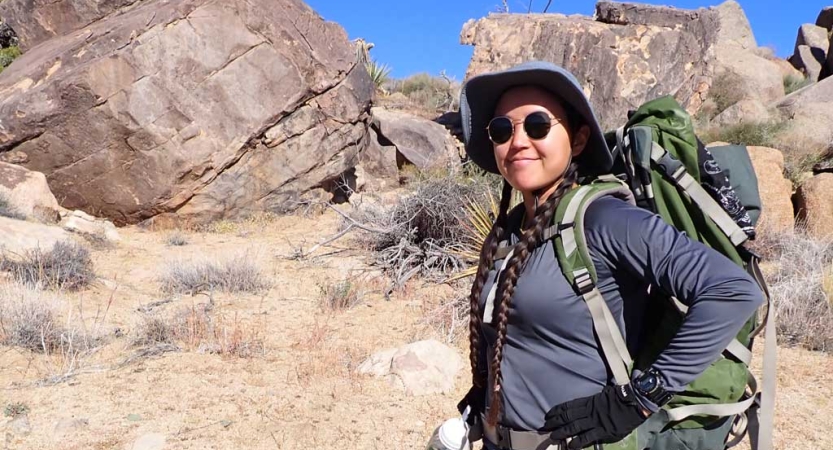 A person wearing a backpack smiles in a desert landscape. 